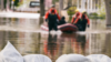 Sandsäcke im Vordergrund und Menschen mit Schlauchboot im Hintergrund