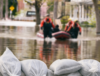 Sandsäcke im Vordergrund und Menschen mit Schlauchboot im Hintergrund